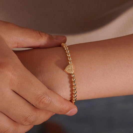 Gold beaded bracelet with a heart-shaped clasp on a white background