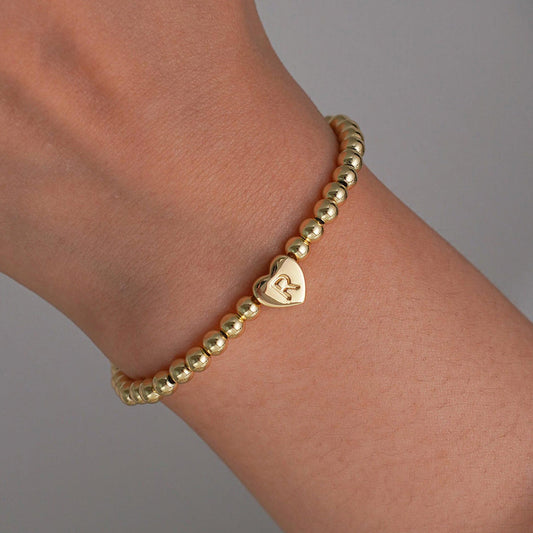 Gold beaded bracelet with a heart-shaped clasp on a white background