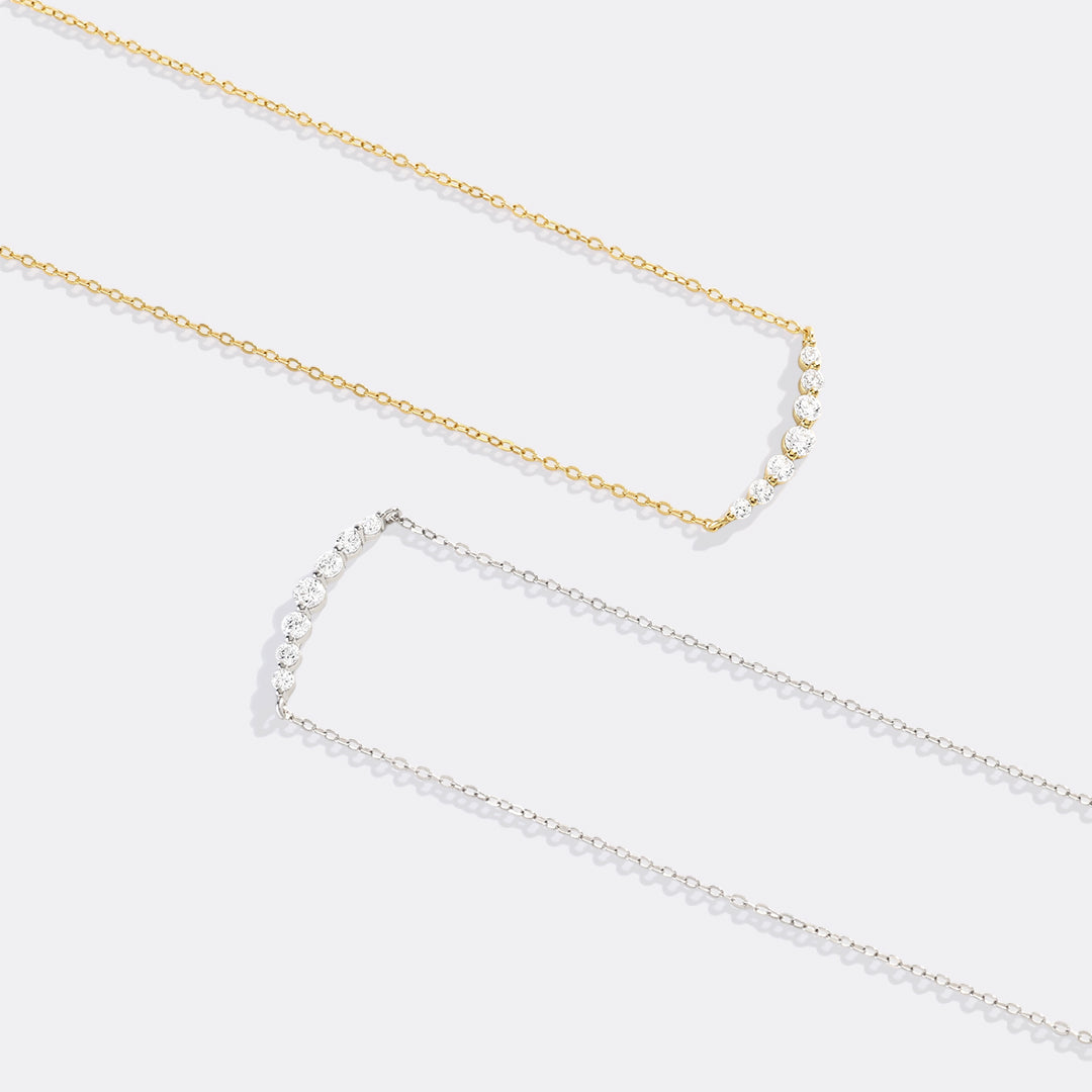 Two pearl necklaces, one gold and one silver, on a light gray background.