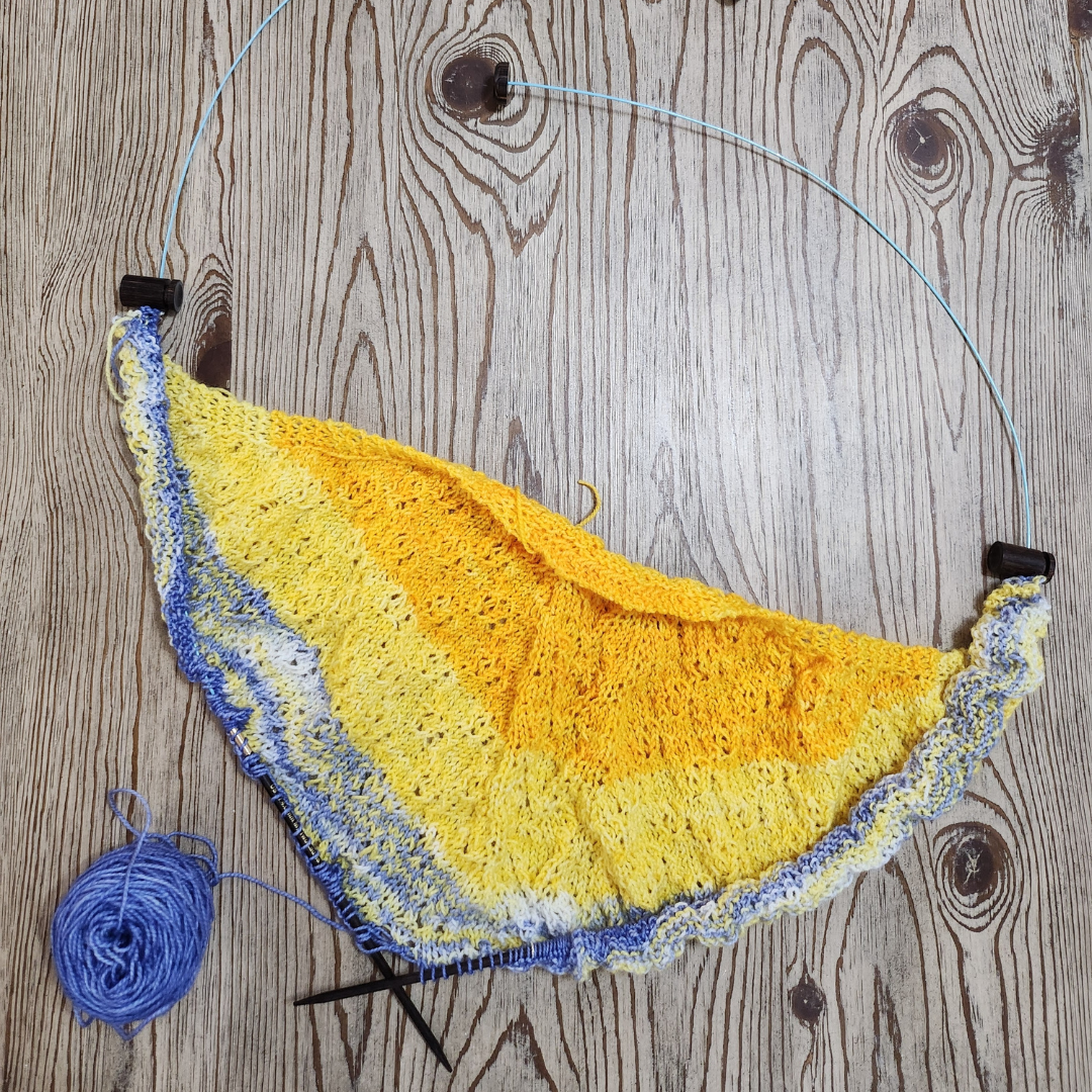 Knitted yellow and blue dishcloth on a wooden surface with a ball of yarn.