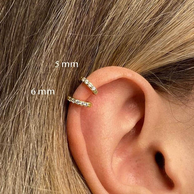 Close-up of an ear with two gold hoop earrings labeled '5 mm' and '6 mm'.