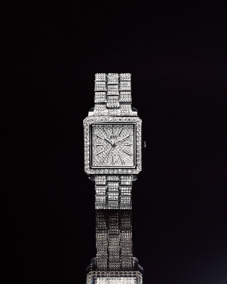 A luxury diamond-encrusted wristwatch with a square silver-toned case and matching diamond-embellished bracelet, centered against a solid black background with a reflective surface below.
