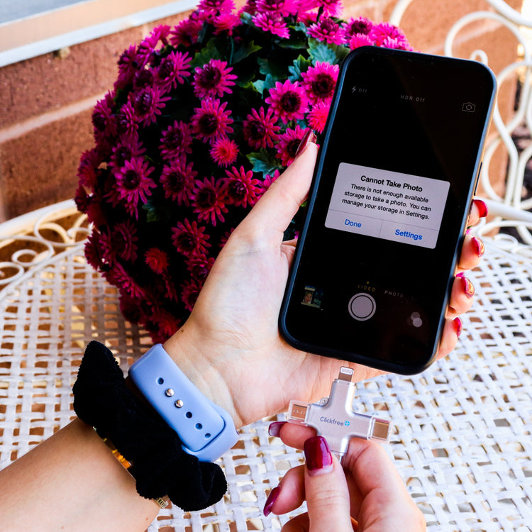 Person holding a smartphone with a camera app error message, next to a bouquet of pink flowers on a wicker table.