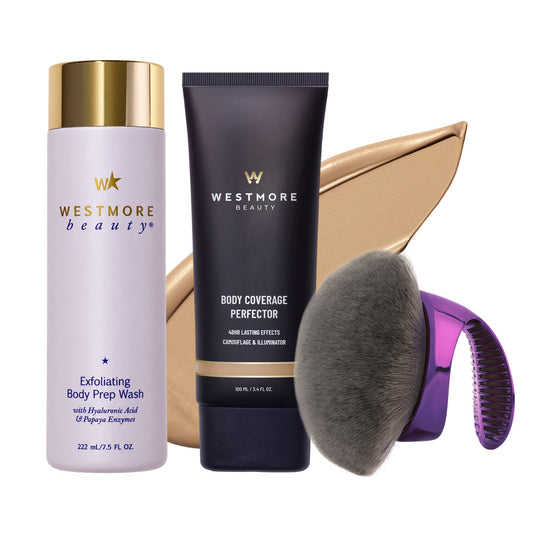 Westmore Beauty hair care set featuring Exfoliating Body Prep Wash in a lavender bottle with a gold cap, Body Coverage Perfector in a dark navy tube with a gold band, a large makeup brush, and a purple-to-pink gradient hair comb, arranged against a white background with a beige makeup smear behind them.