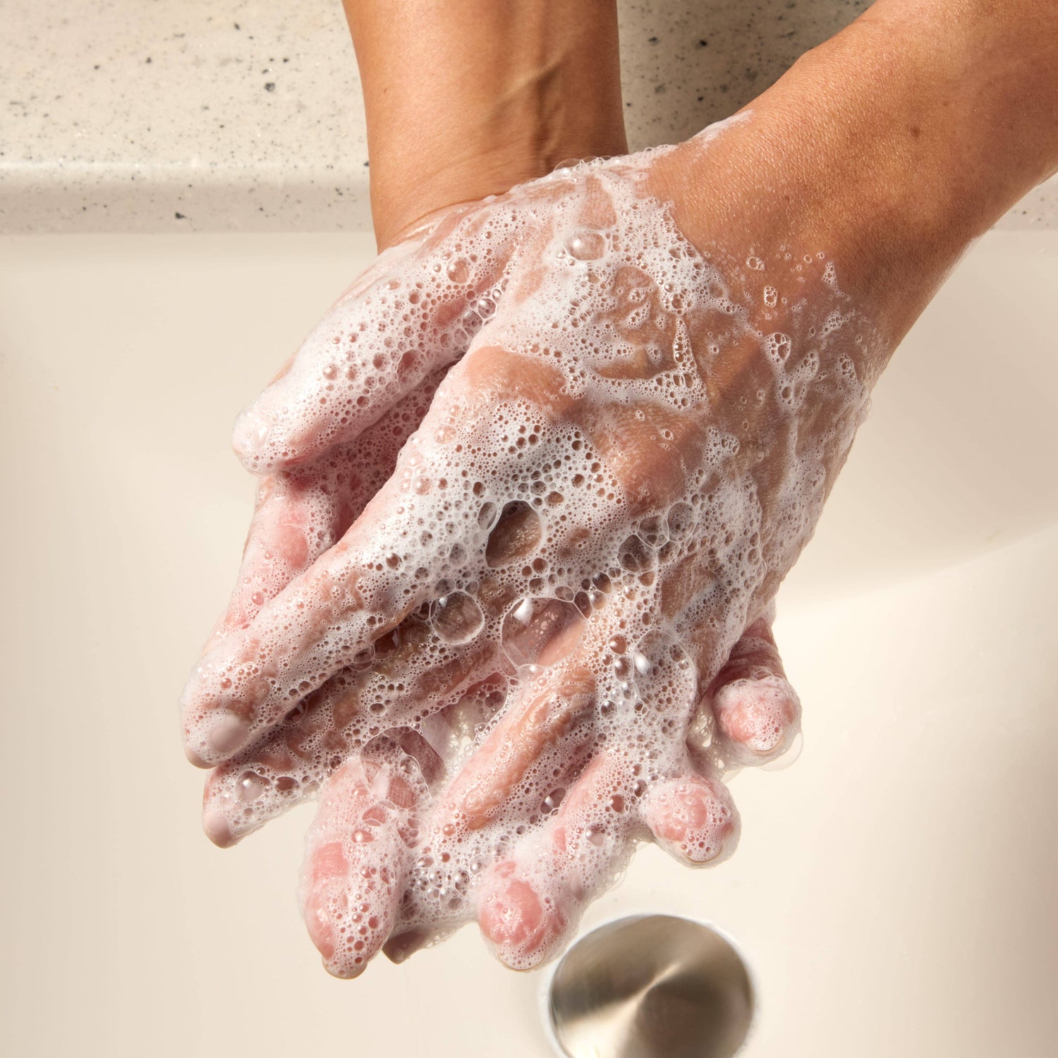 Hands being washed with soap and water in a sink.