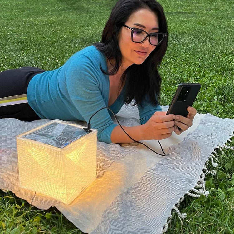 Woman charging phone in park using MEGAPUFF solar lantern on warm light
