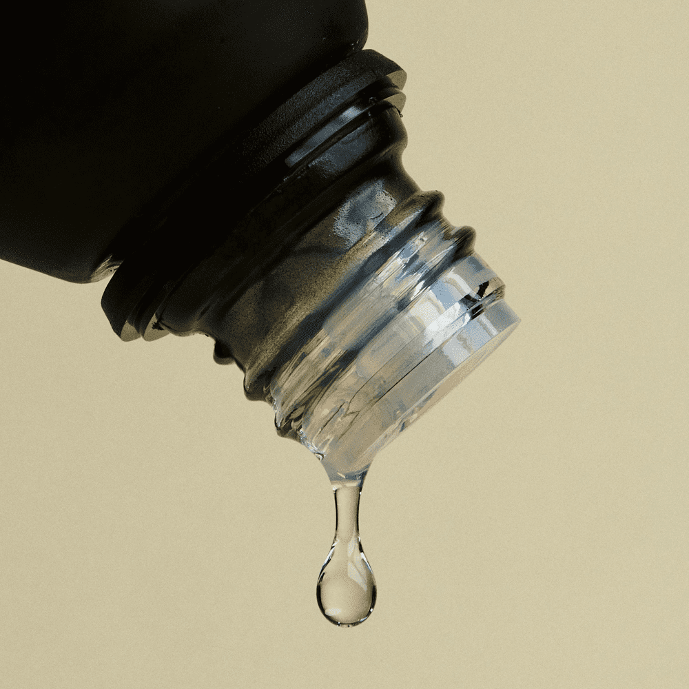 Close-up of a dropper bottle with liquid dripping against a beige background