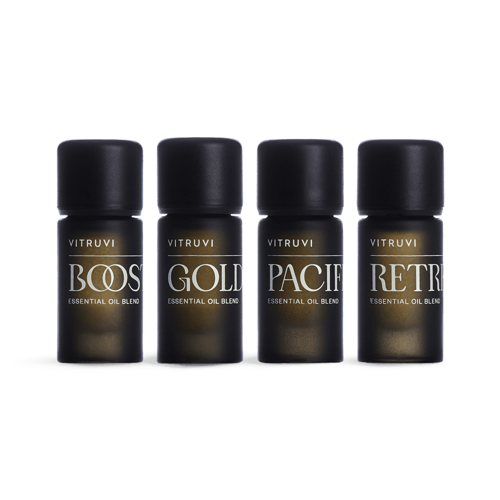 Four Vitruvi essential oil blend bottles labeled 'Boost', 'Gold', 'Pacify', and 'Retr' on a green background.