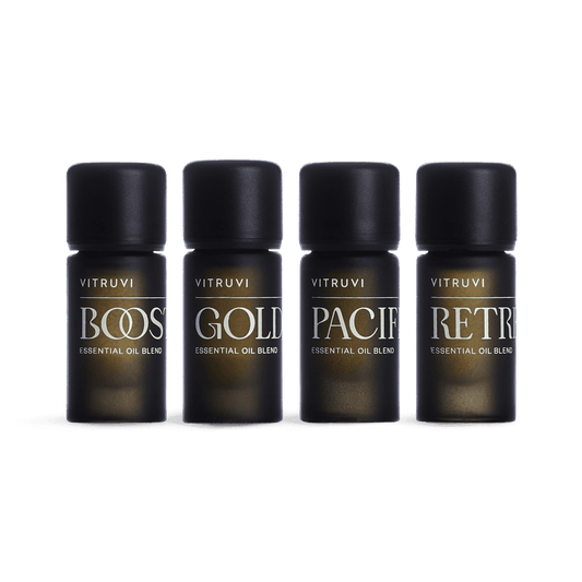 Four Vitruvi essential oil blend bottles labeled 'Boost', 'Gold', 'Pacify', and 'Retr' on a green background.