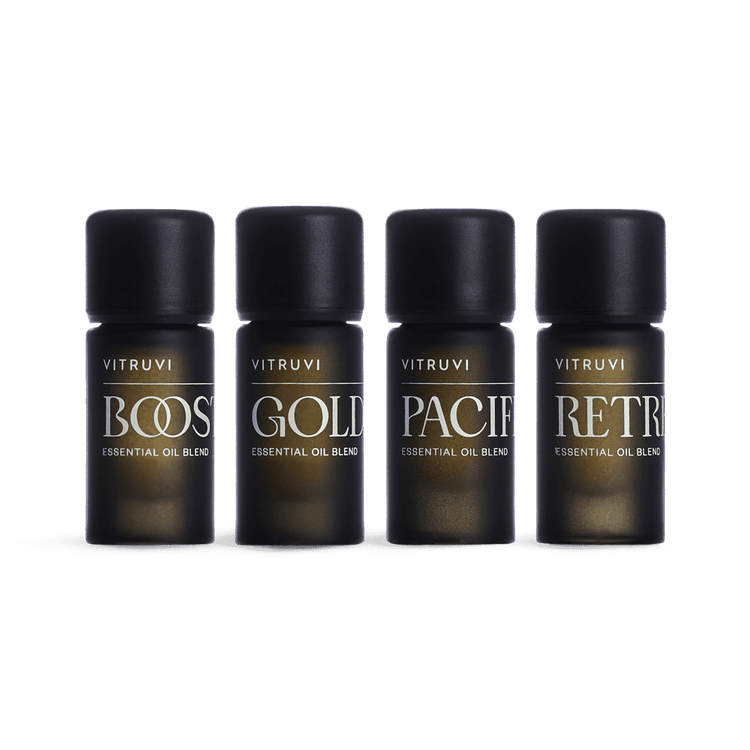 Four Vitruvi essential oil blend bottles labeled 'Boost', 'Gold', 'Pacify', and 'Retr' on a green background.