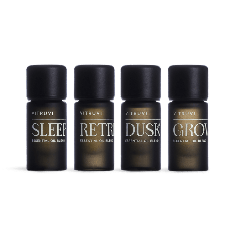 Four Vitruvi essential oil bottles labeled 'Sleep', 'Retreat', 'Dusk', and 'Grow' on a green background.