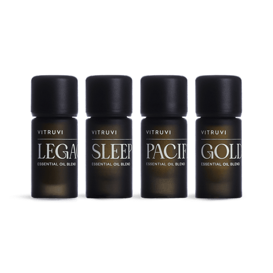 Four Vitruvi essential oil bottles labeled 'Legacy', 'Sleep', 'Pacify', and 'Gold' on a green background.