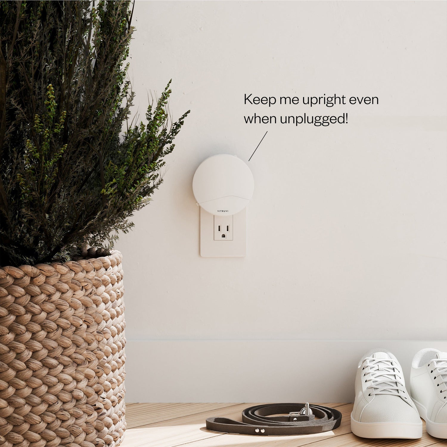 Wall-mounted light fixture with text 'Keep me upright even when unplugged!' next to a plant, shoes, and belt on a wooden floor.