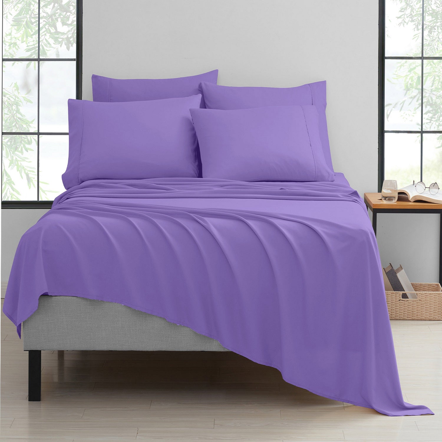 Purple bedding set on a bed in a room with large windows.