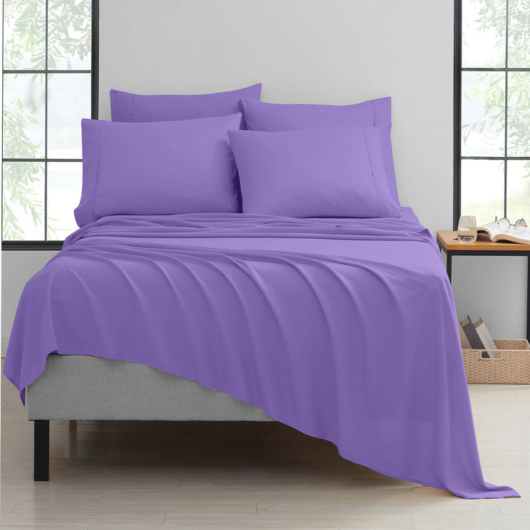 Purple bedding set on a bed in a room with large windows.