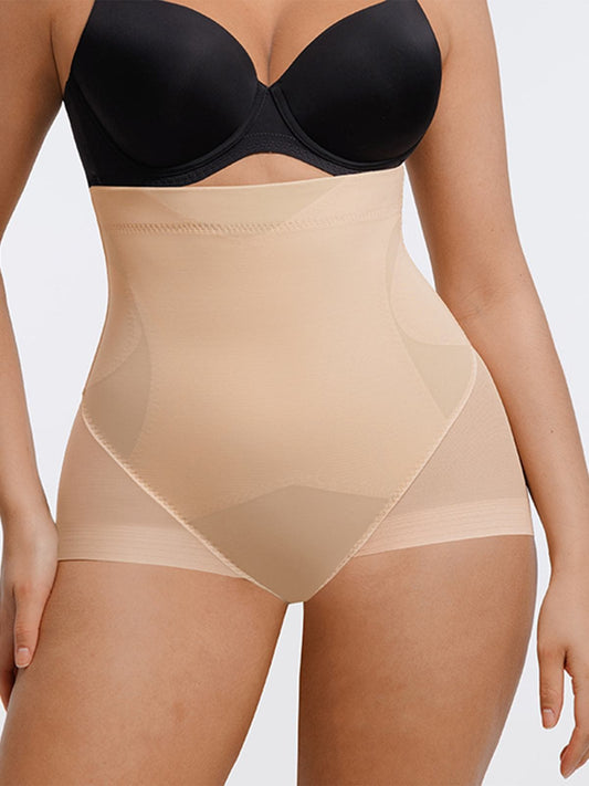 A close-up of a model wearing high-waisted beige shapewear briefs with a black bra, shown against a light gray studio background.