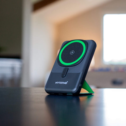 A black NYTSTND Pulse Power Bank with a green accent on the magnetic charging surface, standing upright with an adjustable kickstand.