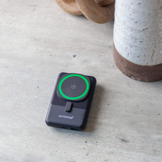 A black NYTSTND Pulse Power Bank with a green accent on the magnetic charging surface, standing upright with an adjustable kickstand.