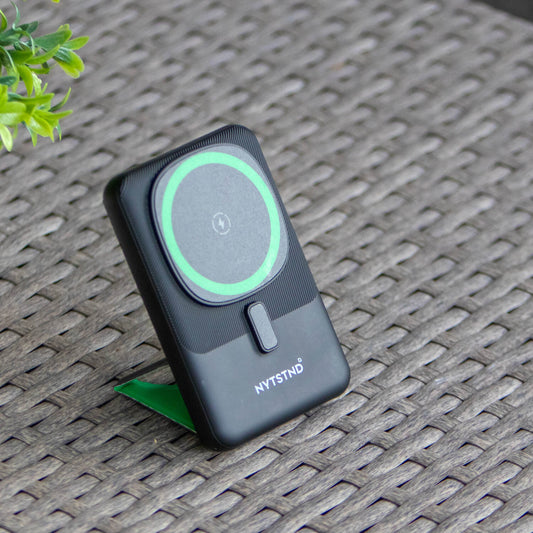 A black NYTSTND Pulse Power Bank with a green accent on the magnetic charging surface, standing upright with an adjustable kickstand.