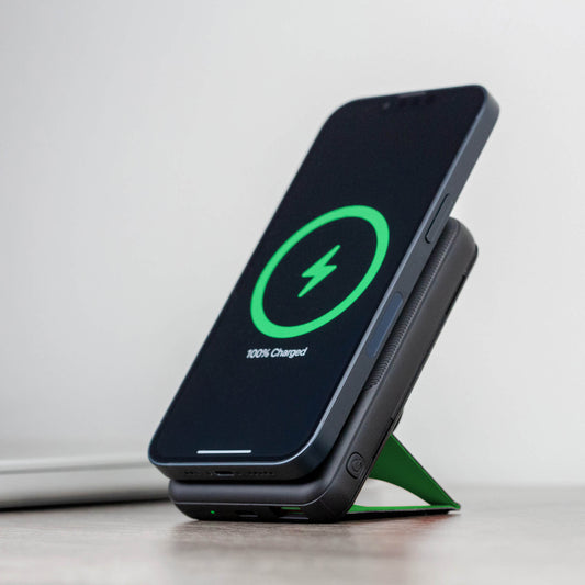 A black NYTSTND Pulse Power Bank with a green accent on the magnetic charging surface, standing upright with an adjustable kickstand.