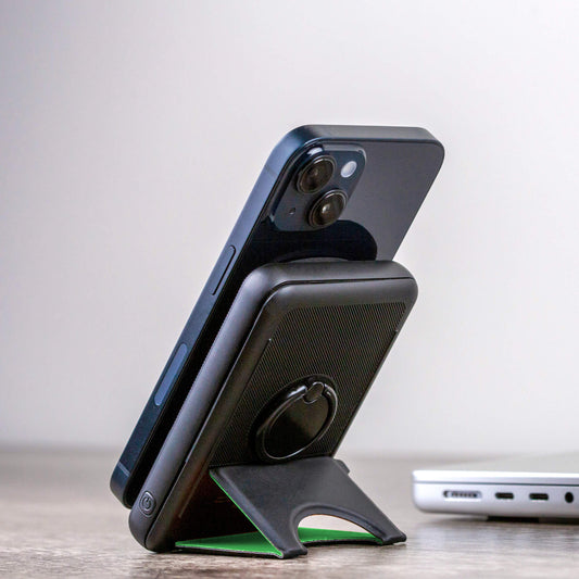 A black NYTSTND Pulse Power Bank with a green accent on the magnetic charging surface, standing upright with an adjustable kickstand.