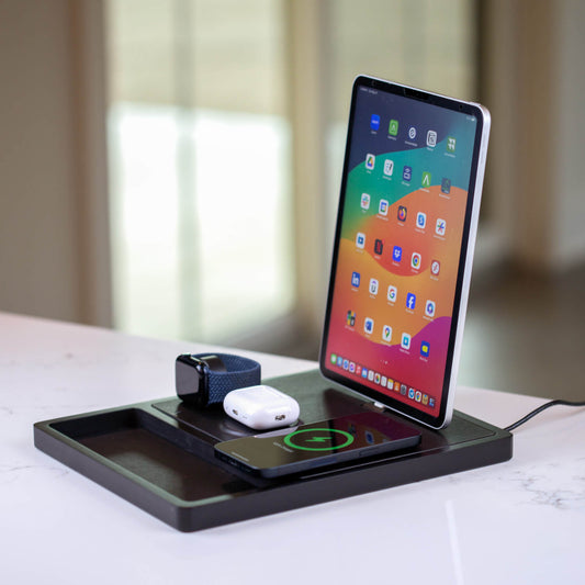 A black 4-in-1 MagSafe wireless charging station with separate sections for charging an iPad, Apple Watch, and other devices, displaying LED indicators.