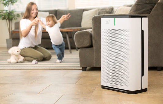 Air purifier on a gray floor with a yellow chair and wooden shelf in the background