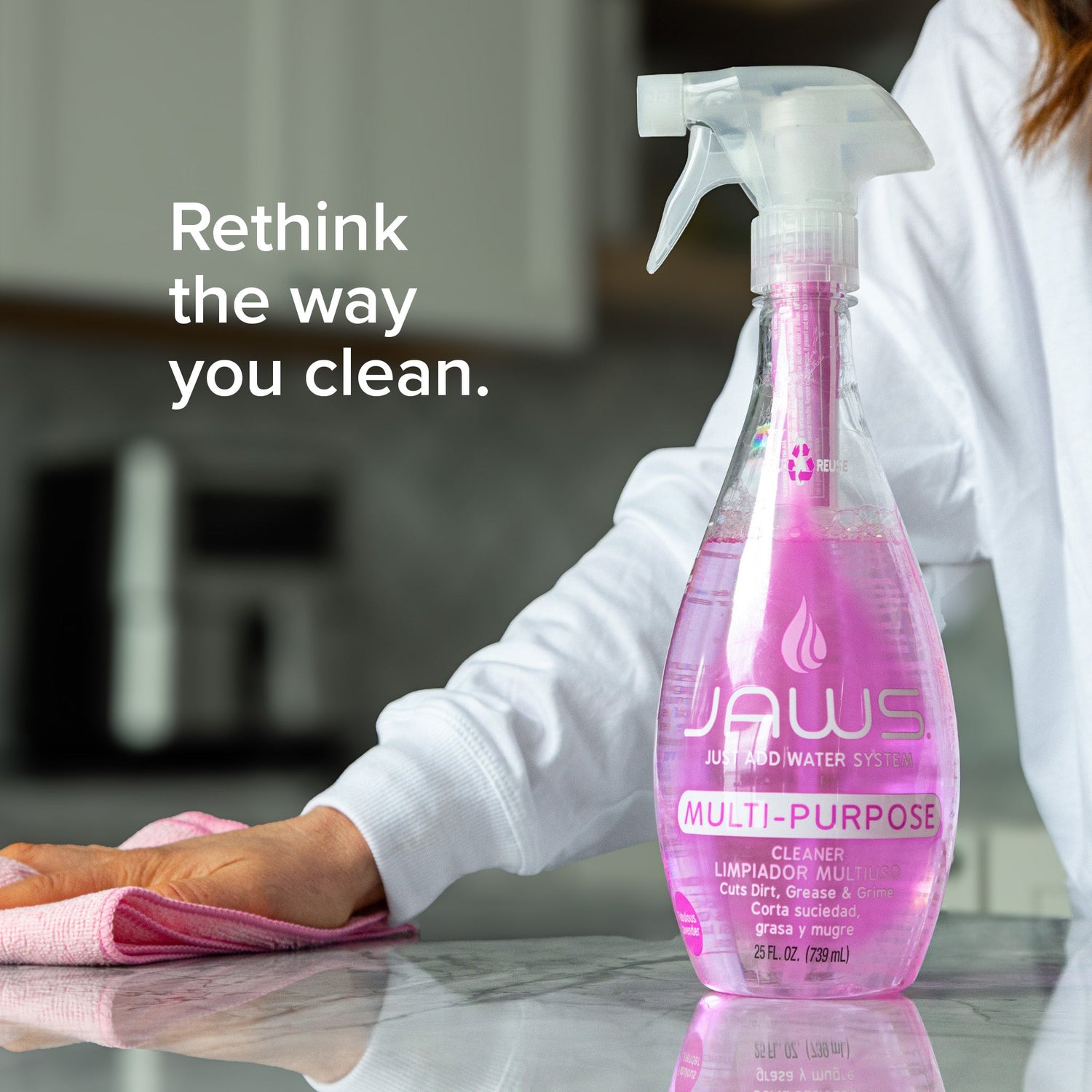 Person cleaning a surface with a pink multi-purpose cleaner bottle labeled 'JAWS' in a kitchen setting.