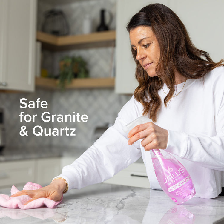 Woman cleaning a kitchen counter with a pink cloth and cleaning solution bottle, text 'Safe for Granite & Quartz' displayed.