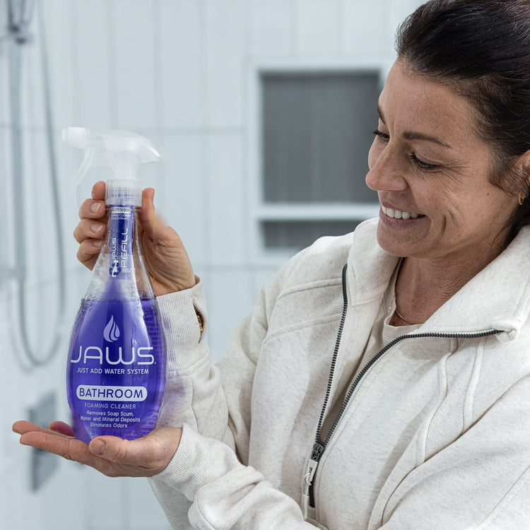 Woman holding a purple bottle of JAWS bathroom cleaner in a bathroom setting