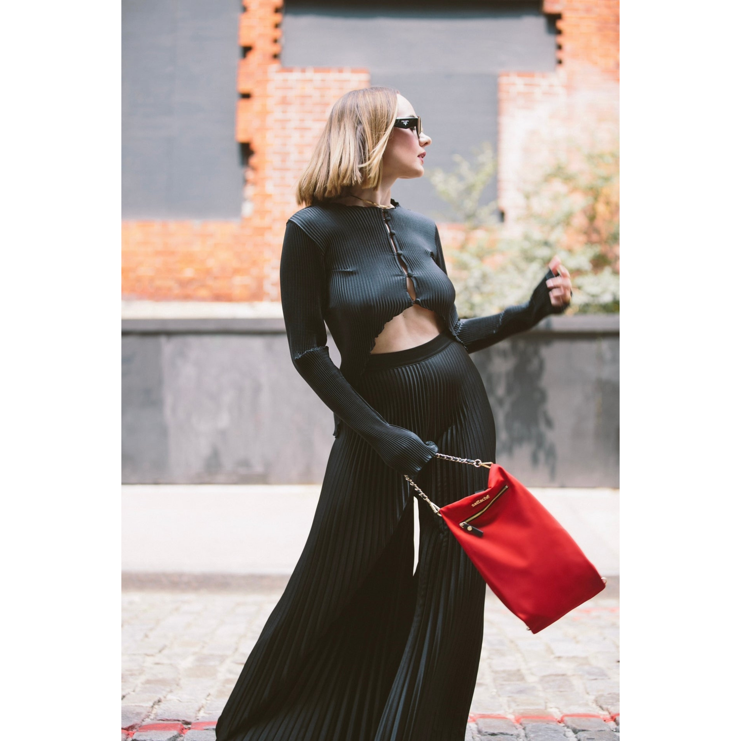 Woman in a black outfit with a red bag standing outdoors.