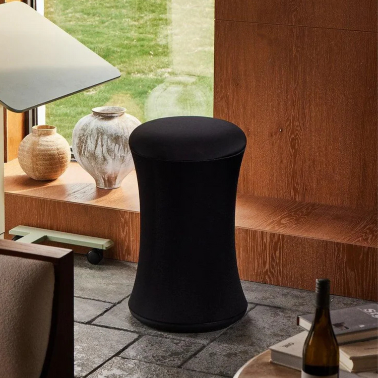 Black covered stool in a room with wooden shelves and decorative items.