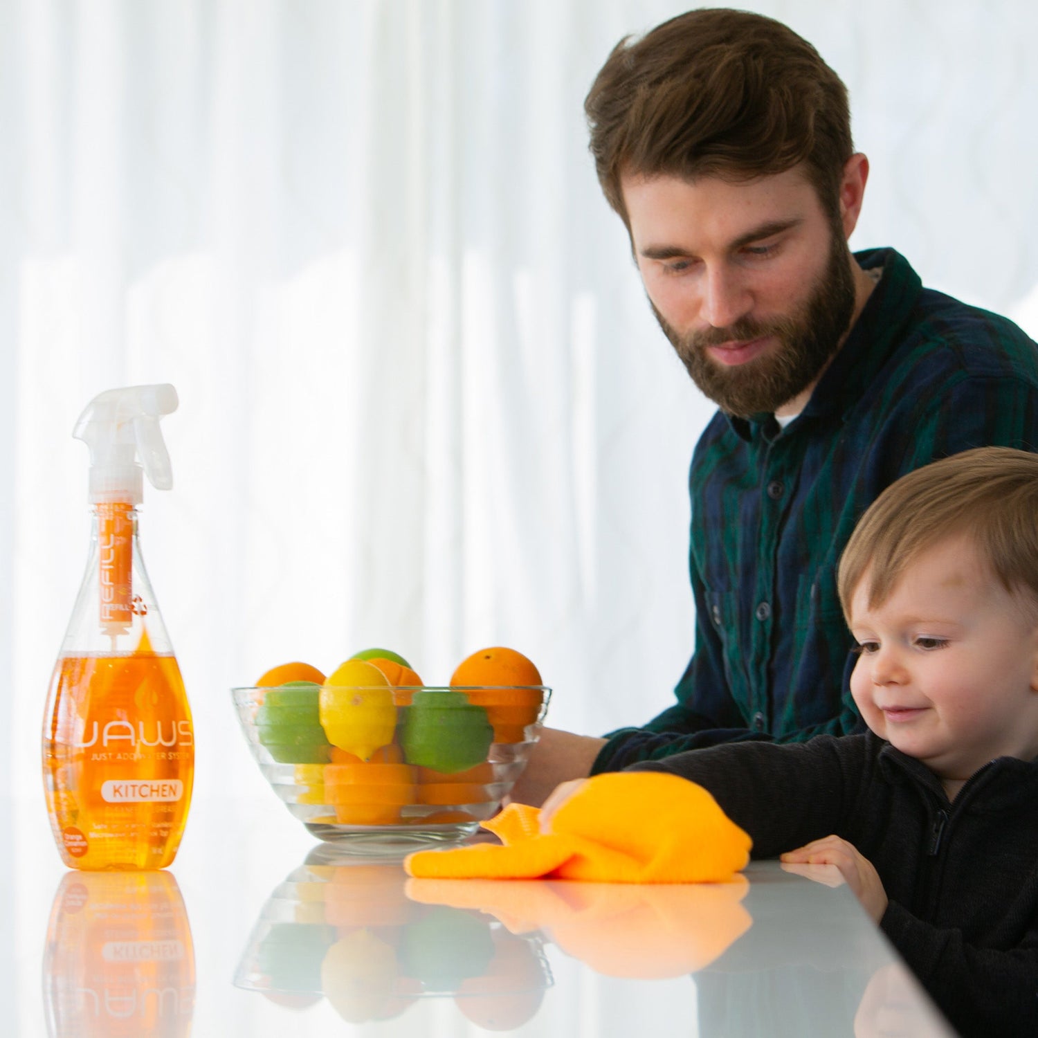 Man and child with a bottle of UAW kitchen cleaner and fruits on a table.