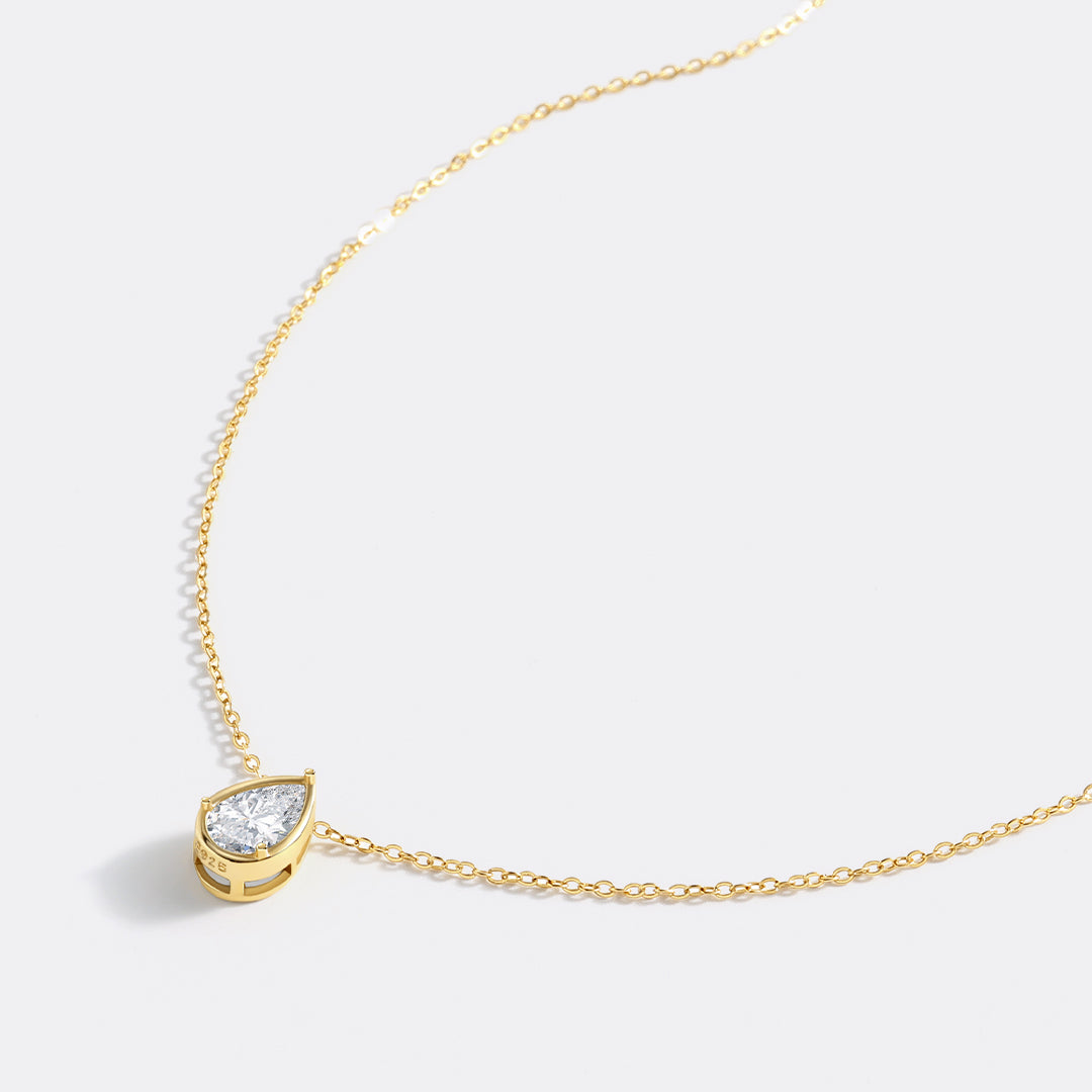 Gold necklace with a teardrop-shaped diamond pendant on a light gray background