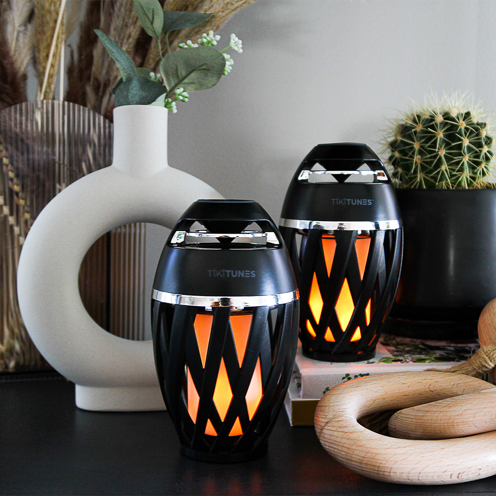 Two decorative lamps with flame-like patterns on a surface with a vase and plant in the background.