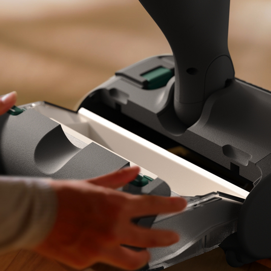 Person using a vacuum cleaner on a wooden floor in a kitchen.