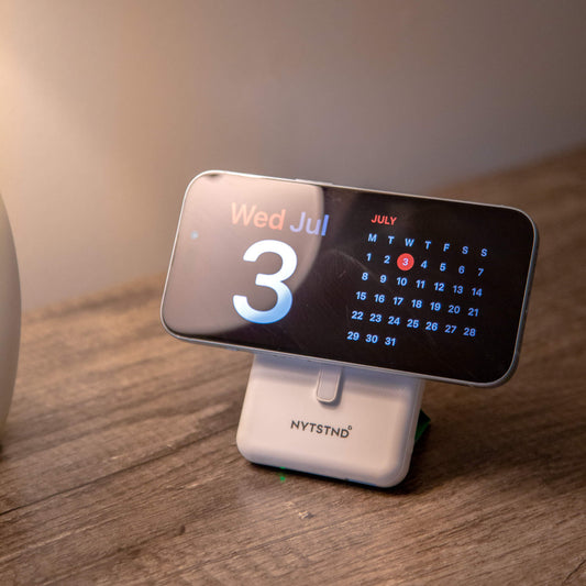 A white NYTSTND Pulse Power Bank with a green circle indicating the magnetic charging area, featuring an adjustable kickstand.