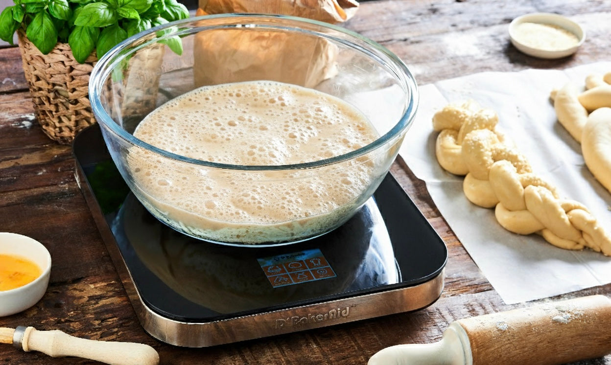 Bowl of risen dough on a digital kitchen scale with bread-making ingredients on a wooden table.