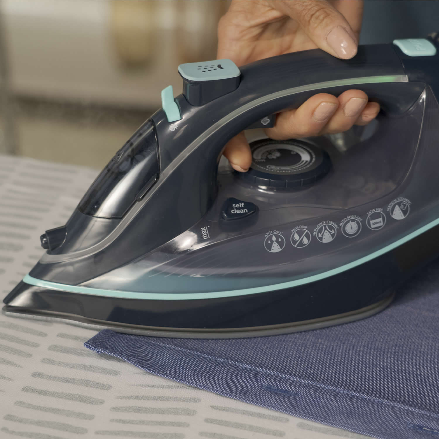 Person ironing fabric with a modern steam iron on a table.