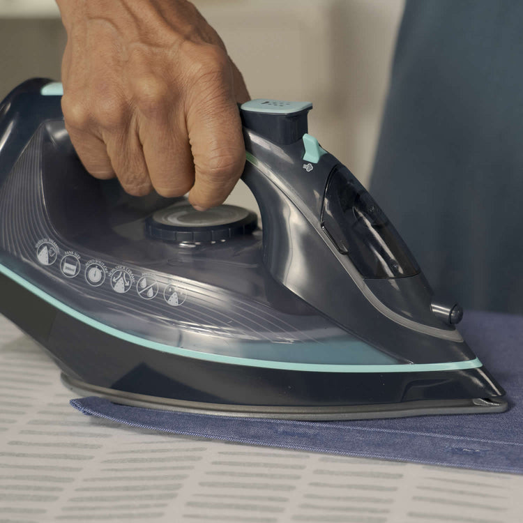 Person ironing fabric with a modern steam iron on a flat surface.