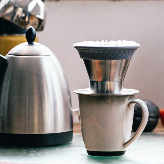 Pour over coffee dripper on top of a coffee mug next to a brew kettle